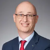 Christian Scherm, Landesgeschäftsführer Finanzen und Administration, im dunkelblauen Anzug und mit roter Krawatte vor grauem Hintergrund