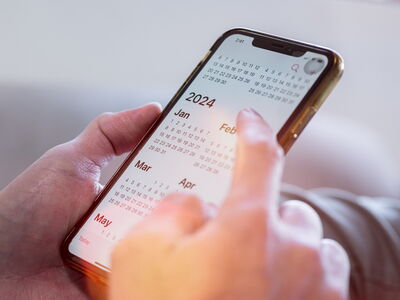 Nahaufnahme eines Smartphones in Männerhänden. Auf dem Display ist ein Kalender zu erkennen.